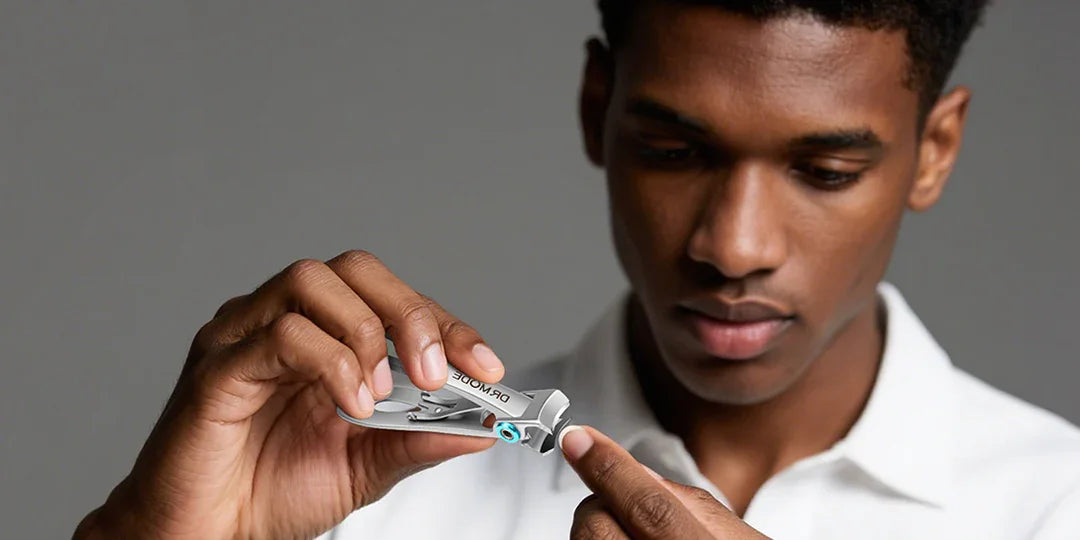 Man using precision stainless steel nail clippers for grooming on gray background.