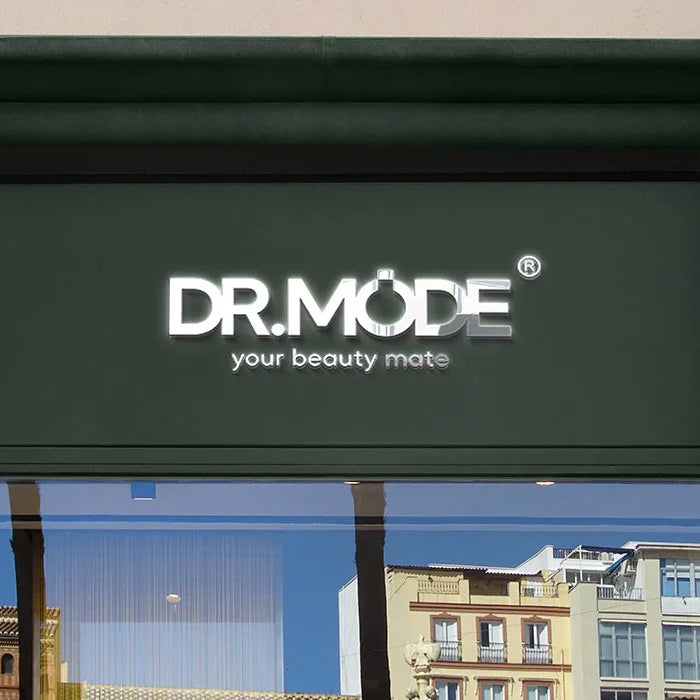 Illuminated storefront sign reading 'DR.MODE your beauty mate' above a large window