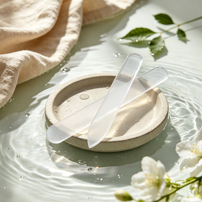 Two gentle crystal glass nail files on ceramic dish with water jasmine flowers, soothing natural nail care spa experience at home